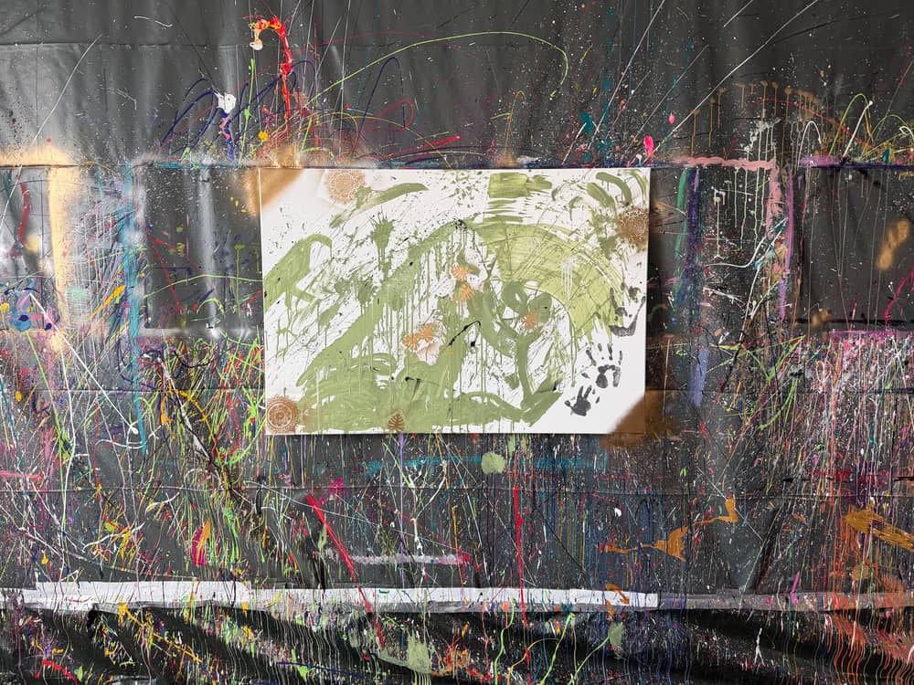 Fertiges grünes Kunstwerk mit Handabdrücken vor der bunten Splash-Wand
